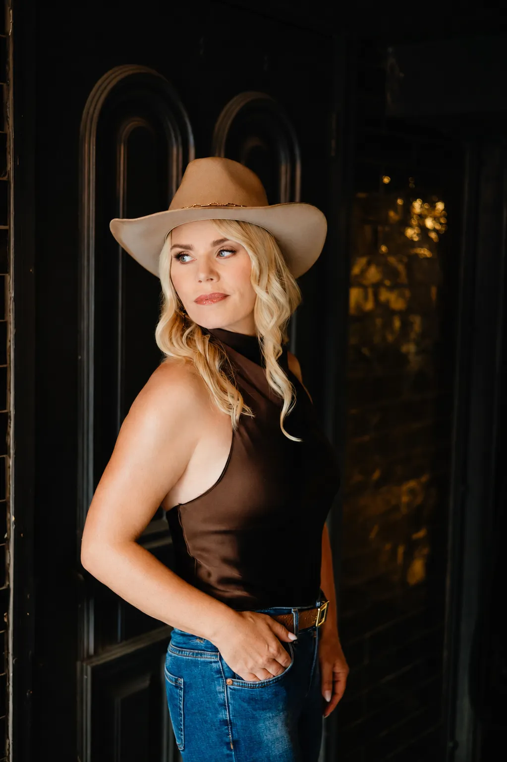 Carina Dahlmann in a hat, glancing over her shoulder against a dark wall