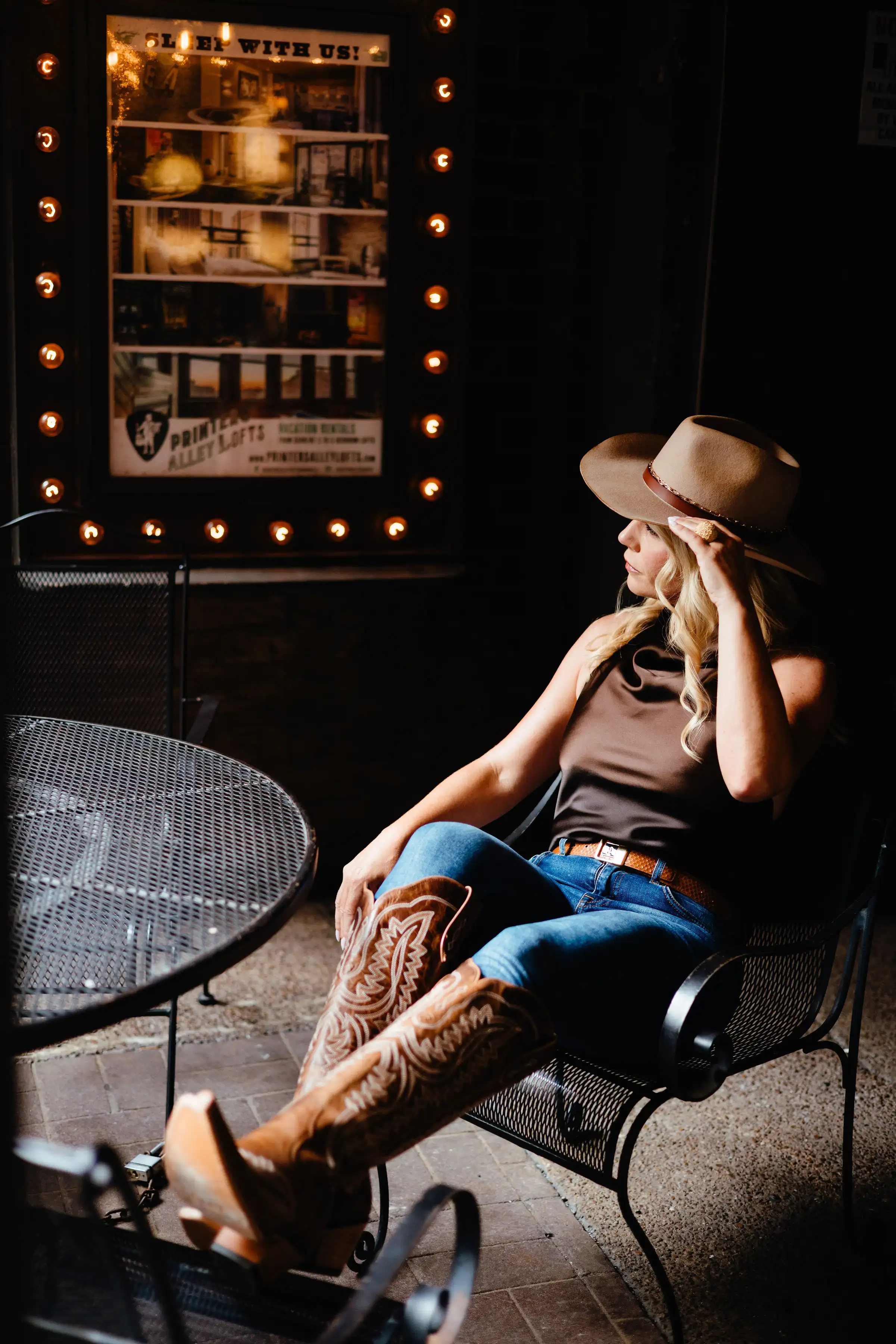 Carina Dahlmann seated in front of a lit Printer's Alley poster, wearing a hat